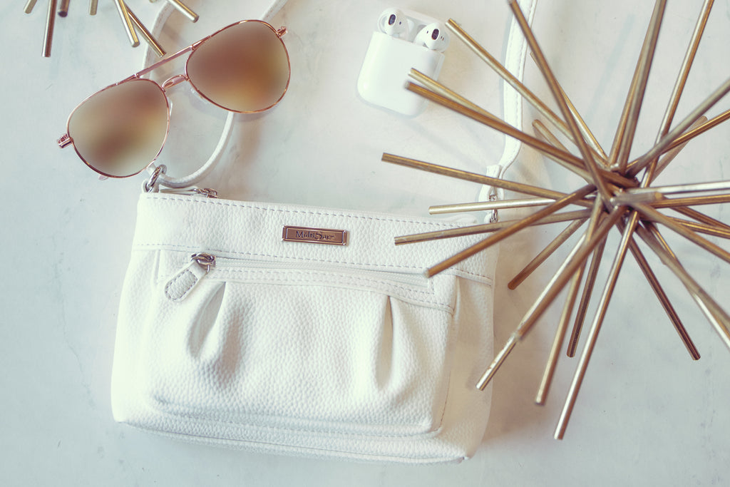 Cruelty Free Bags - Our White Irvine Crossbody Bag rests on a table next to headphones and sunglasses. 