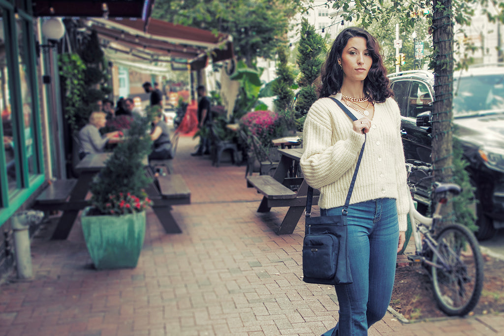 Shopping Tips for This Holiday Season - A woman in a white sweater and jeans walks around town shopping with her reno crossbody bag. 